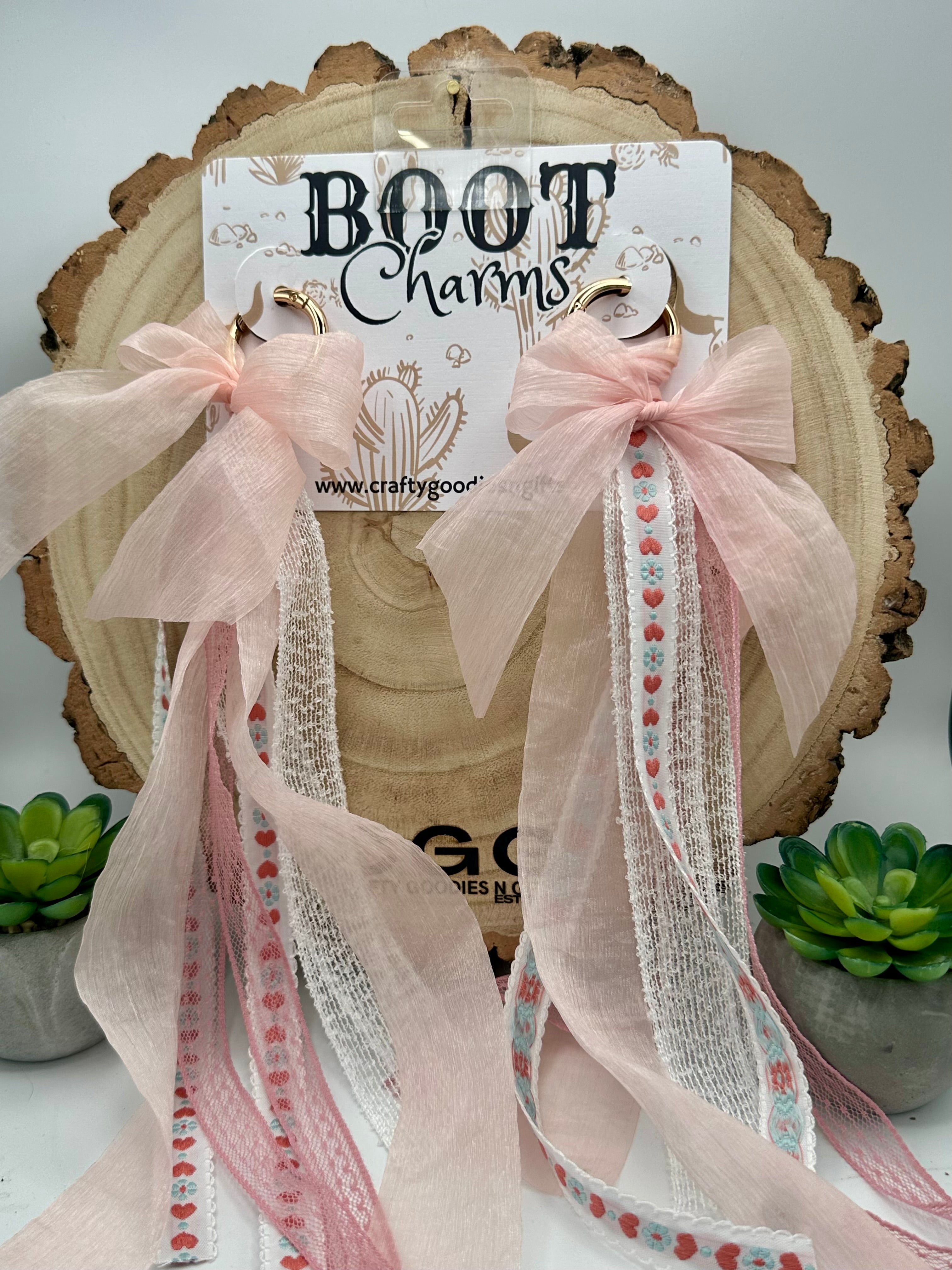 Two pink boot charms with long sheer ribbon tails and patterned trim.