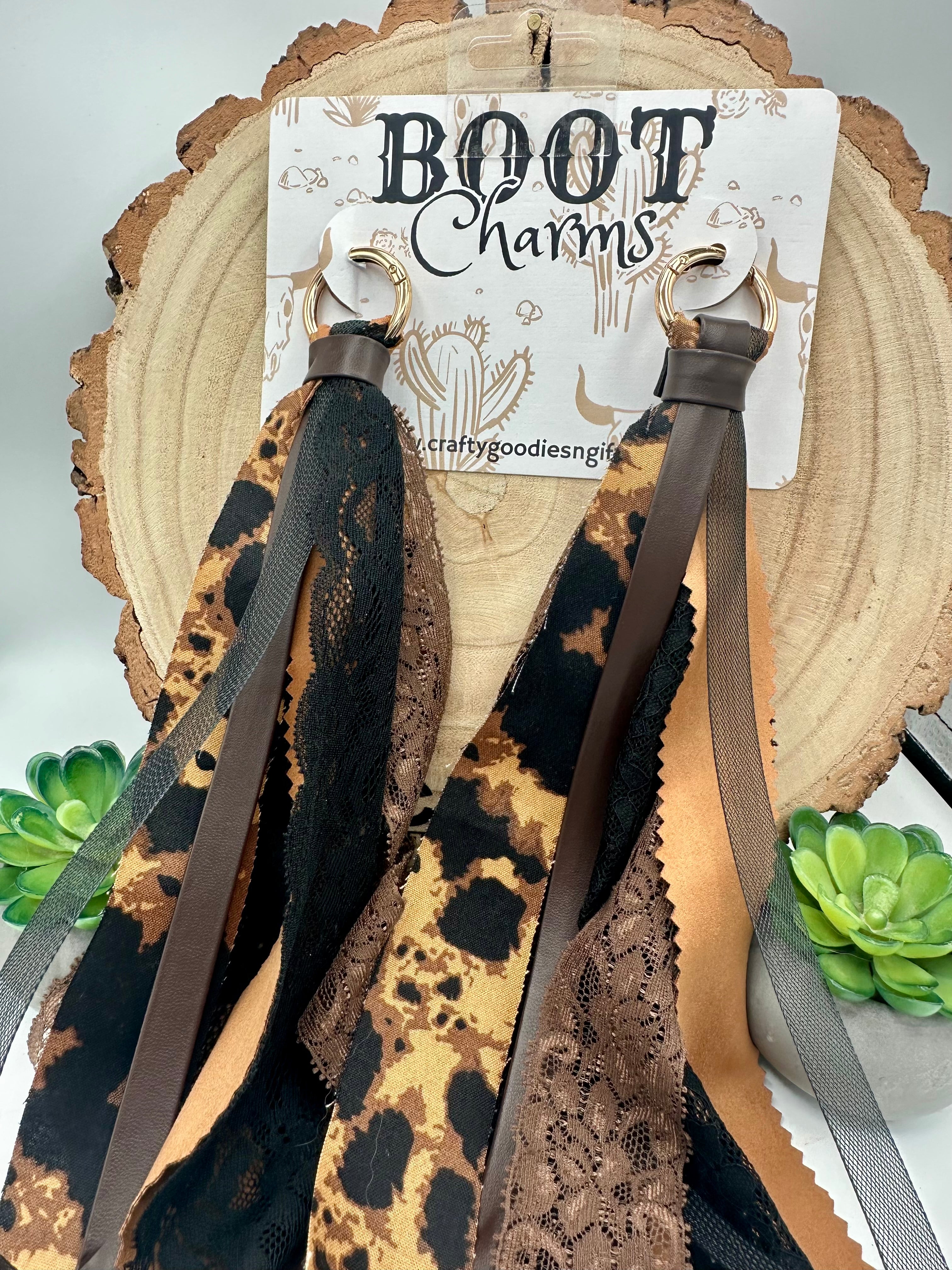 A pair of brown and black lace and leopard-print boot charms with long brown straps.
