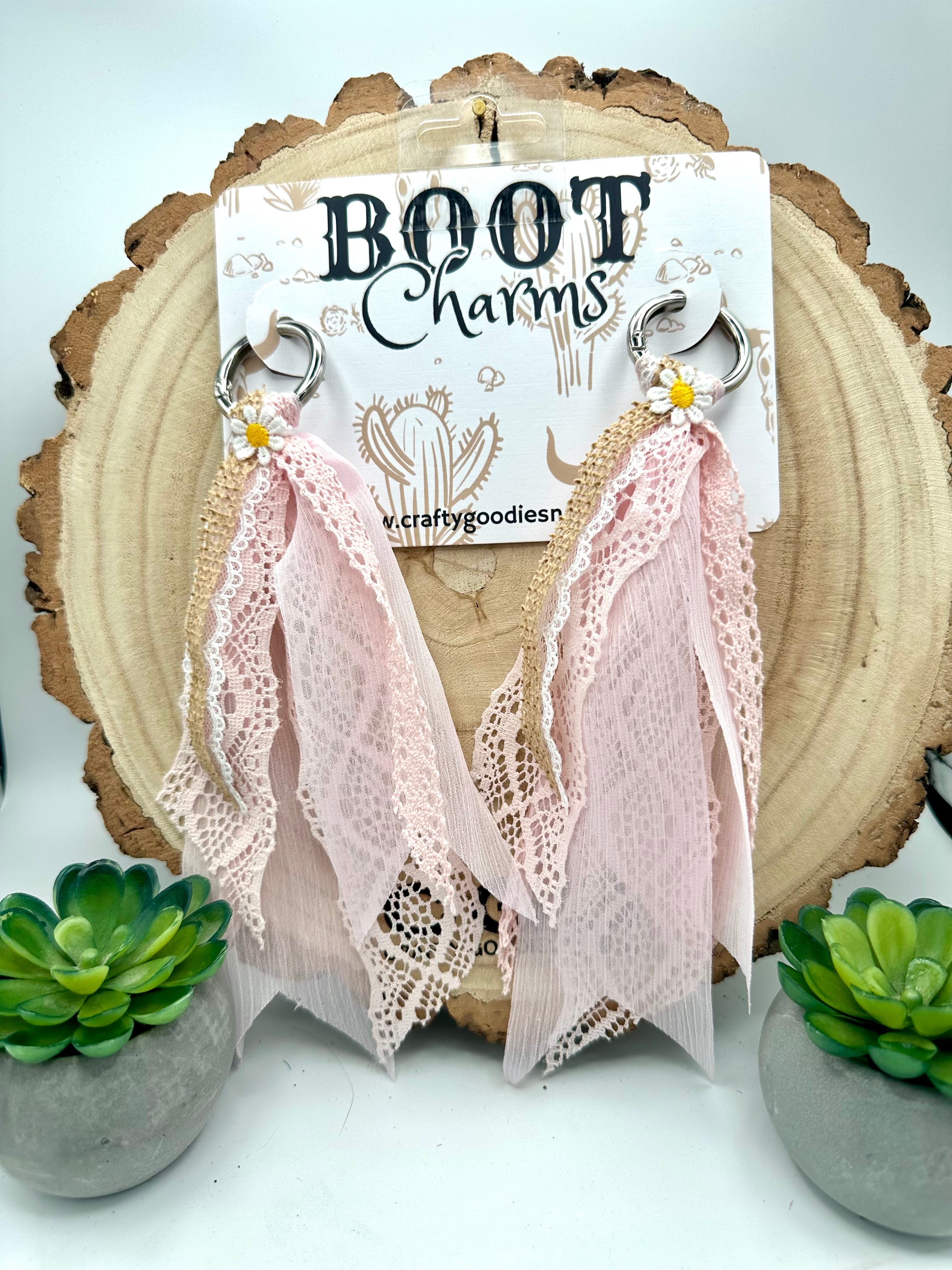 A pair of dangling boot charms with long blush pink lace and ribbon tassels.