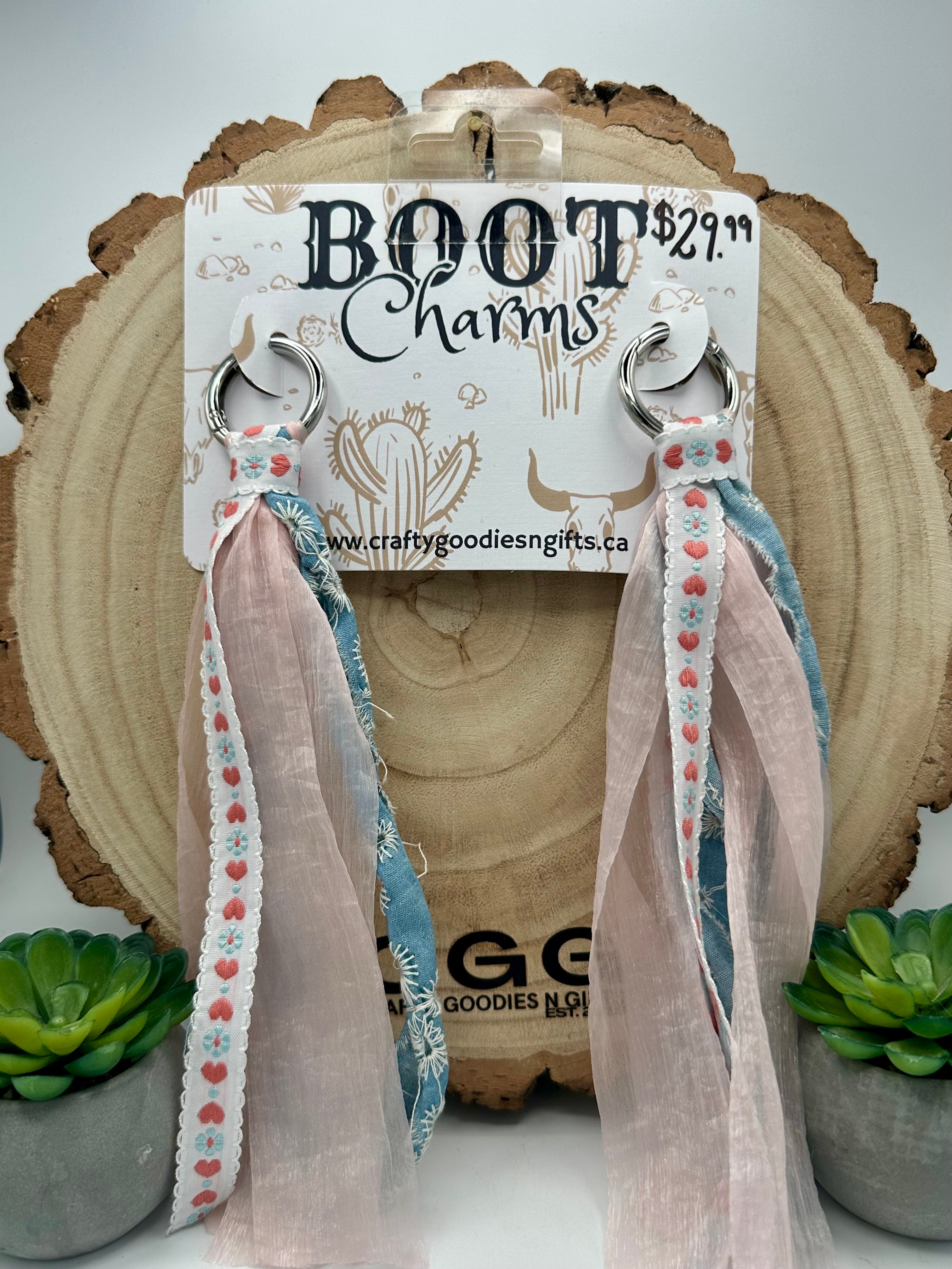 A pair of long dangling boot charms with silver-tone rings, blush pink tulle ribbons, and blue patterned fabric.