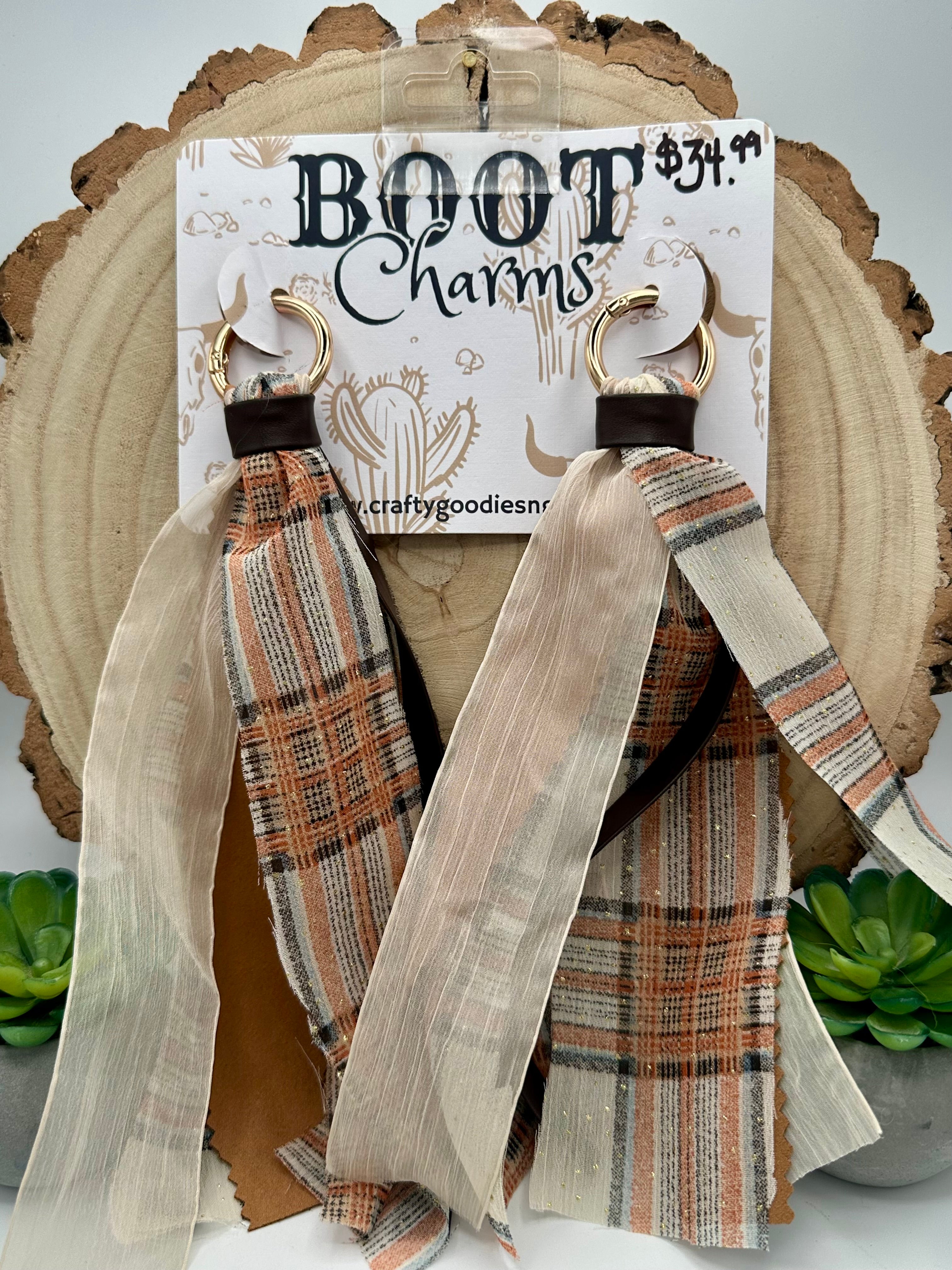 A pair of dangling boot charms featuring plaid ribbon straps in beige, brown, and orange tones with sheer cream ribbons.