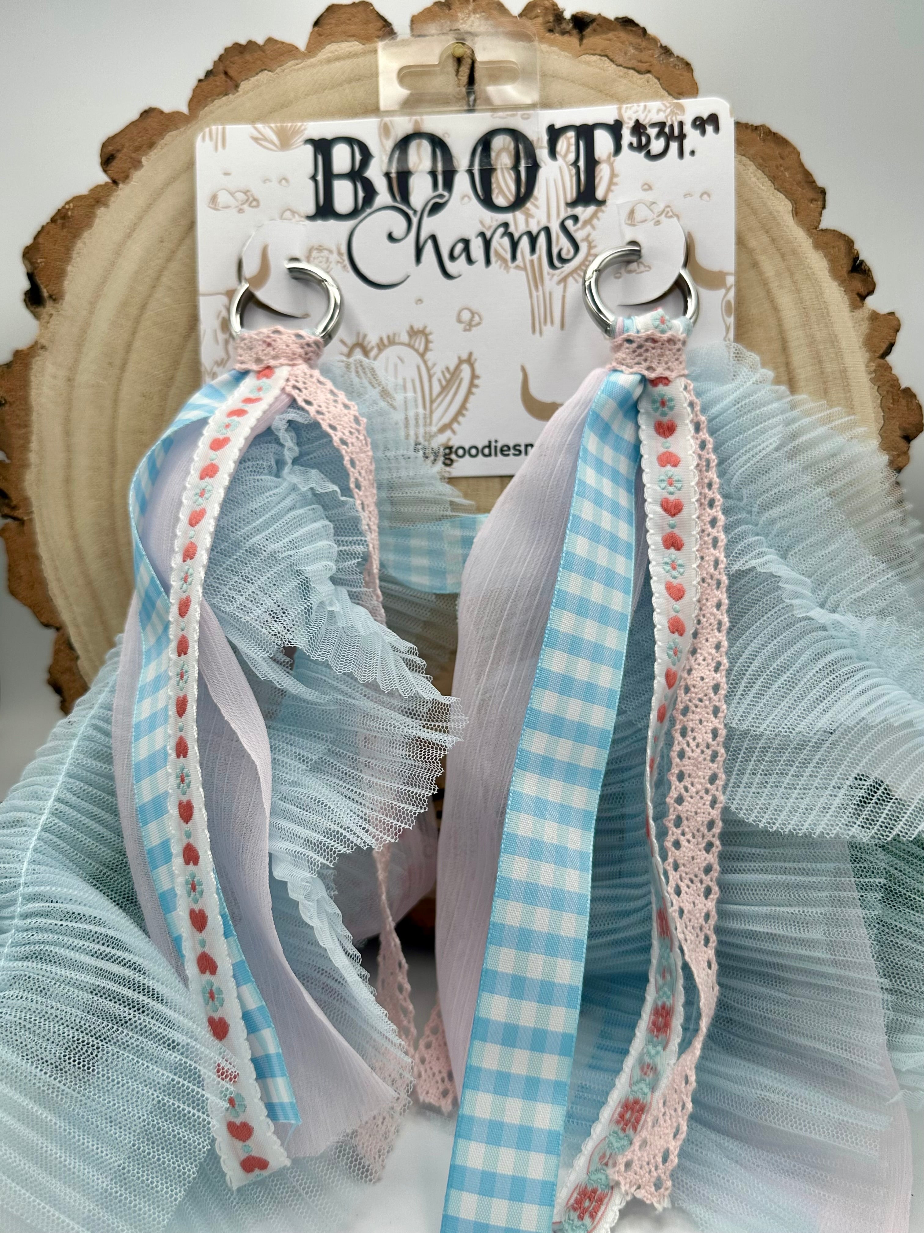 A pair of BOOT Charms. The tassels feature light blue and white gingham, sheer white organza, and pink lace trim with small red hearts.