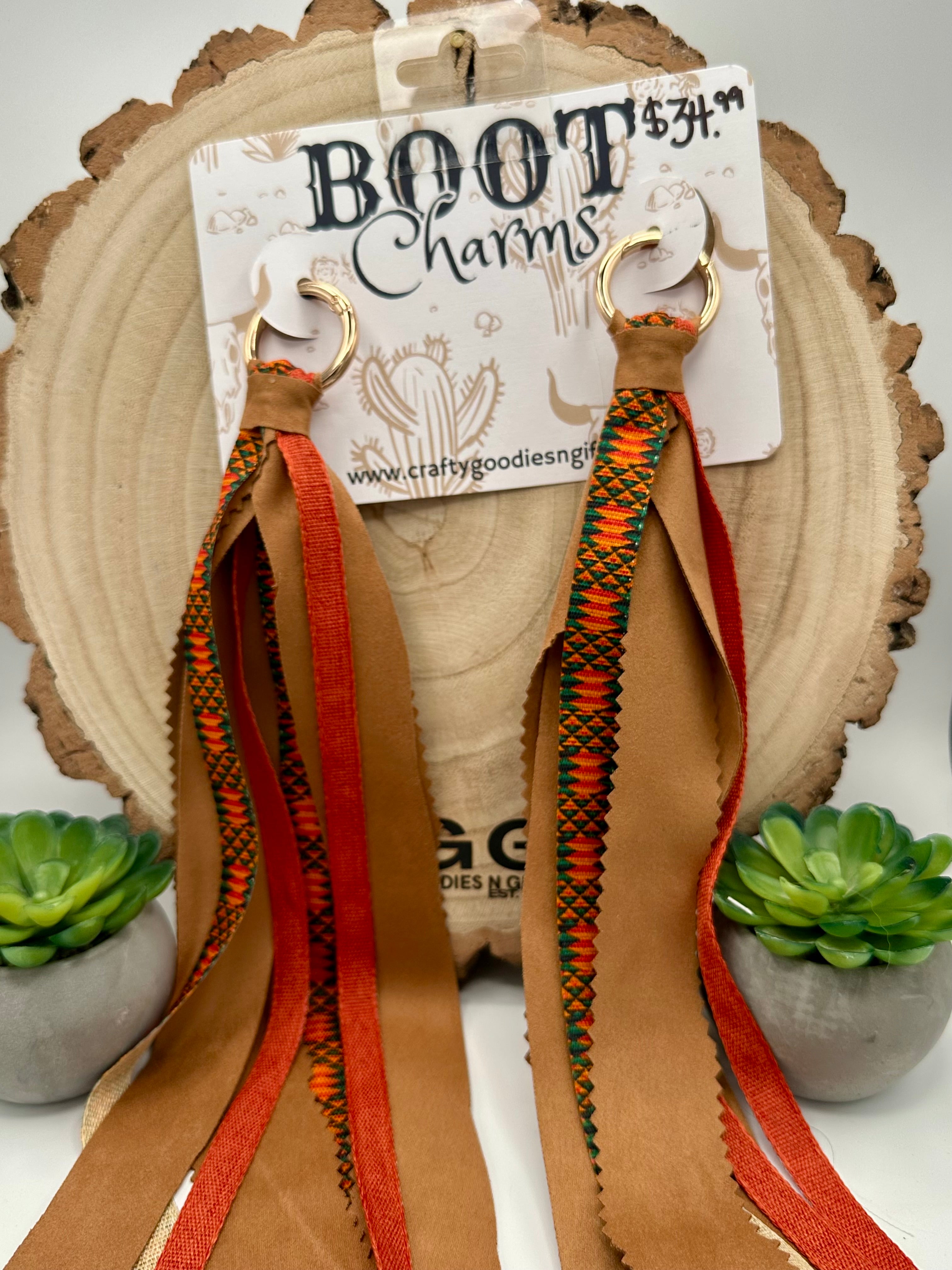 A pair of  BOOT Charms feature tan leather straps with orange, black, and green woven pattern details and gold-tone rings.
