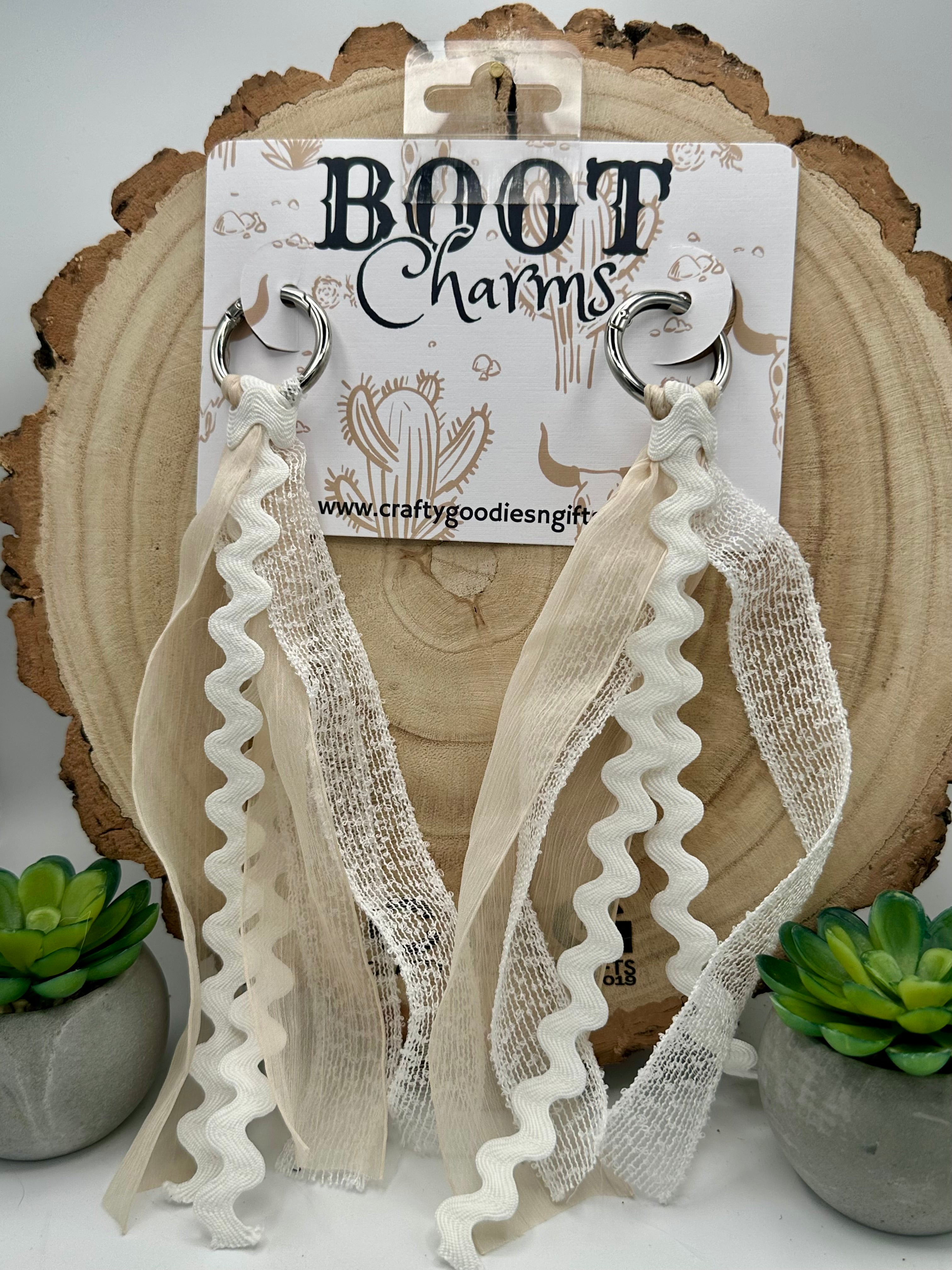 A pair of boot charms featuring cream-colored textured lace and ruffled ribbon loops attached to silver metal rings.