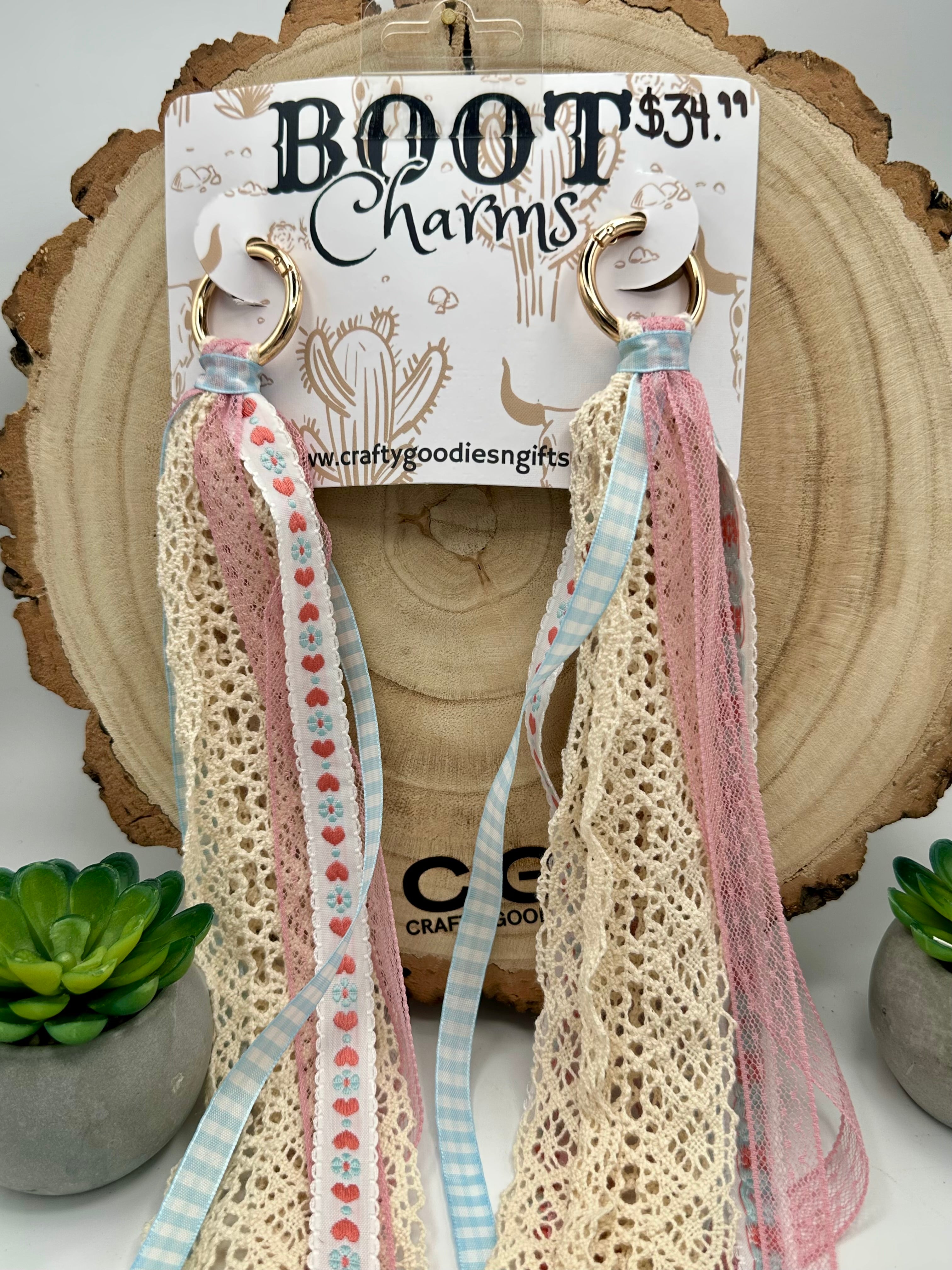 A pair of boot charms that feature cream crochet lace, light pink mesh, and pastel blue and pink ribbons.