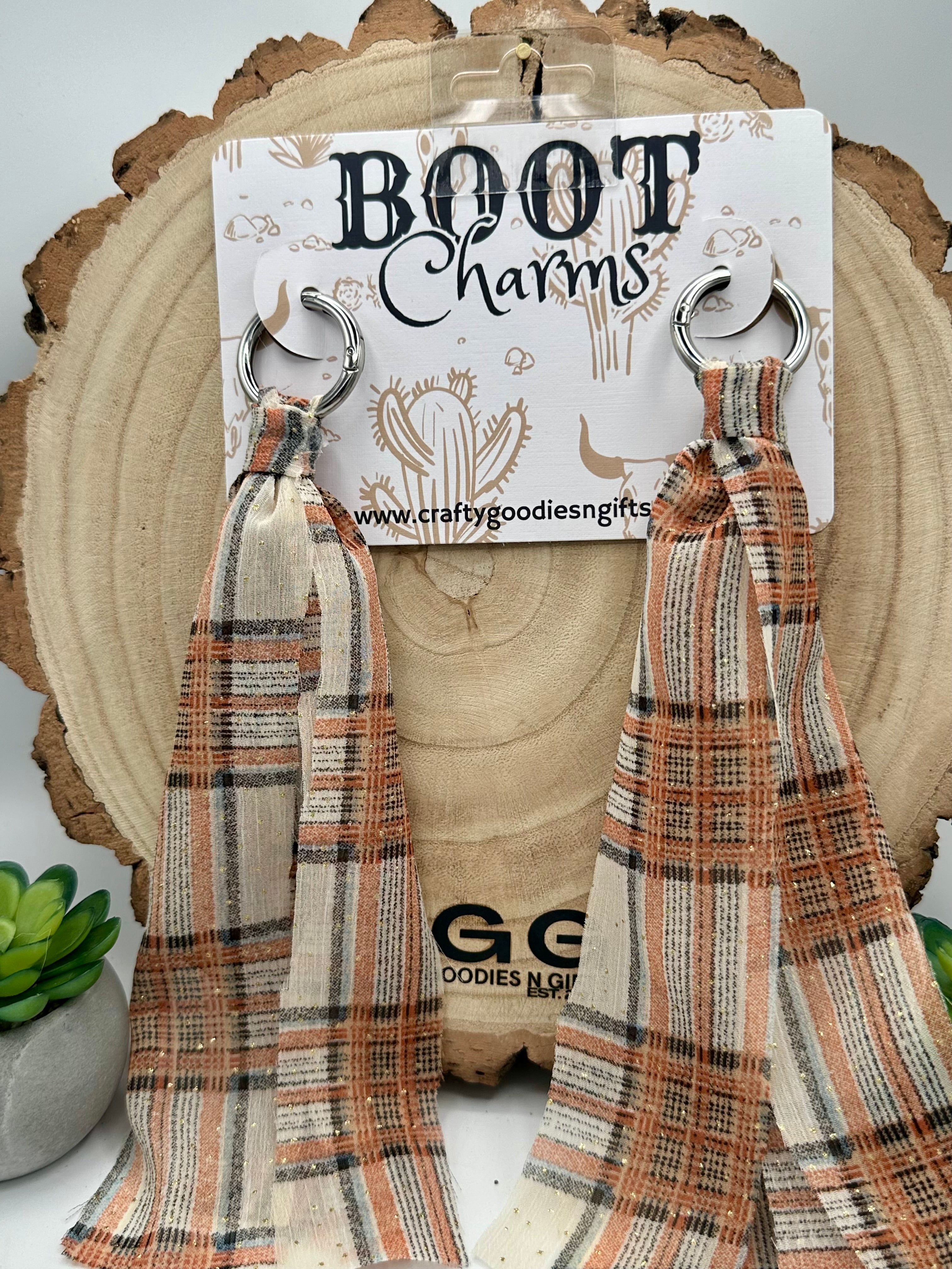 A pair of dangling boot charms with a plaid pattern in beige, brown, and orange, hanging from silver metal rings.