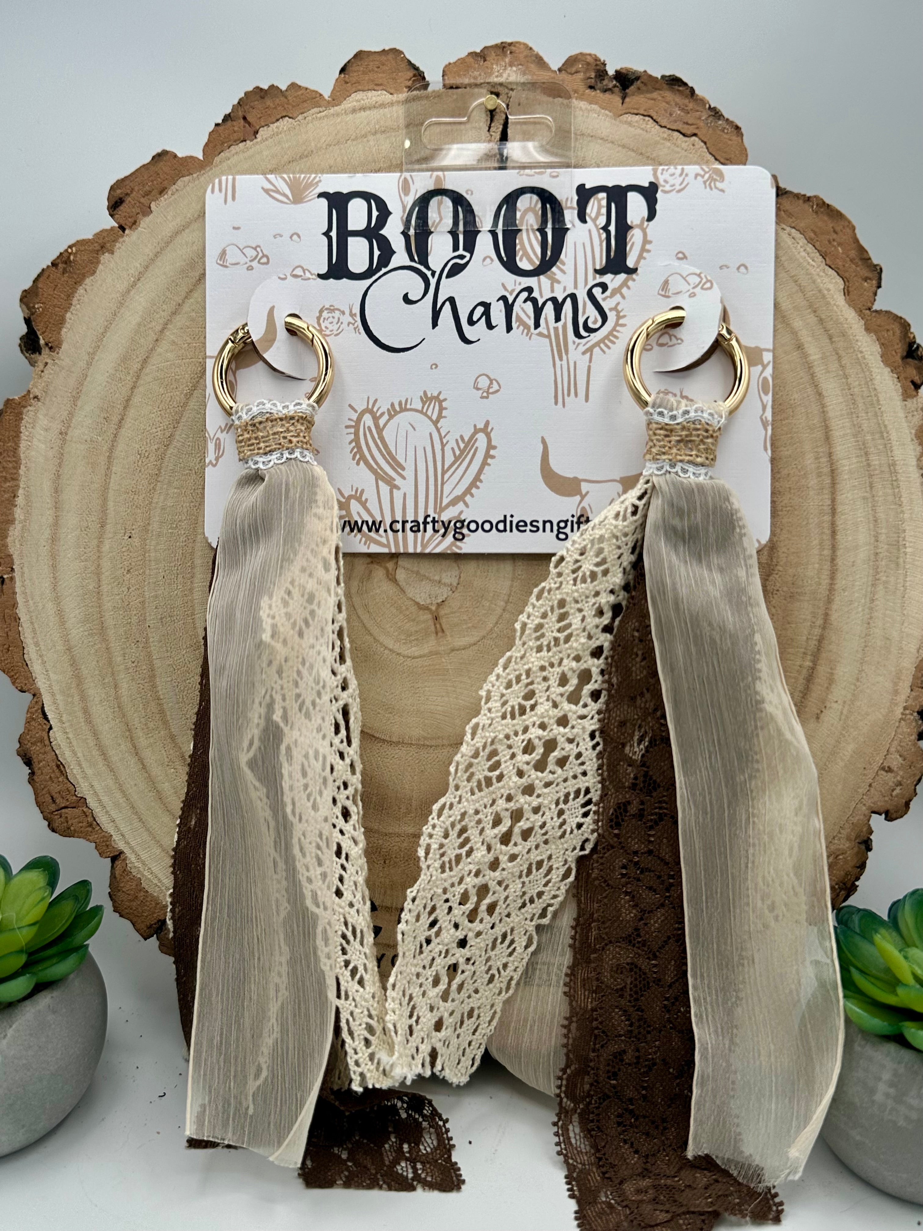 A pair of Boot Charms that have gold-tone hoops with, long sheer taupe-beige ribbon drops, and one lace drop in cream and one in dark brown.