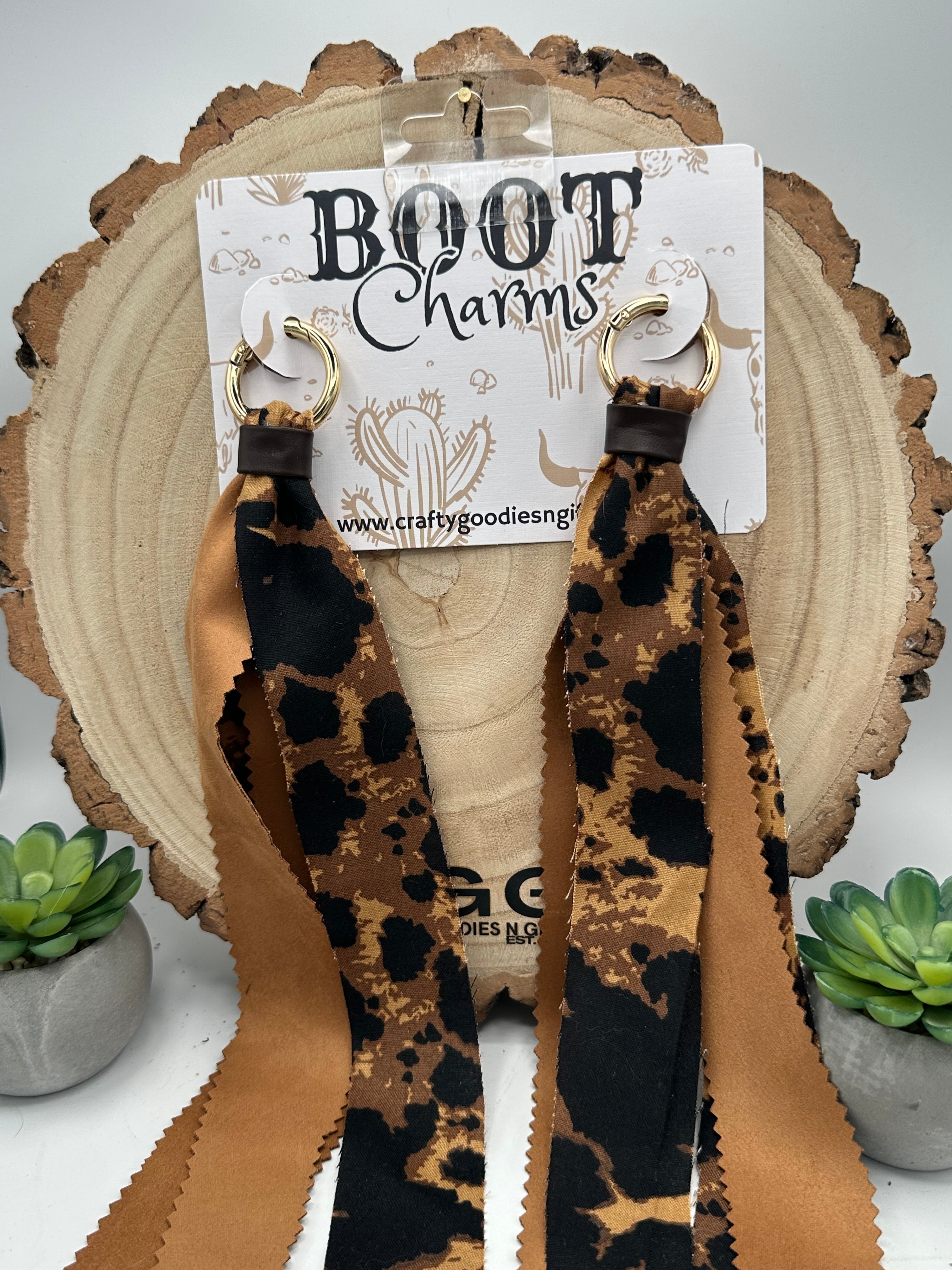 A pair of leopard-print and tan woven boot charms with gold-tone metal rings.