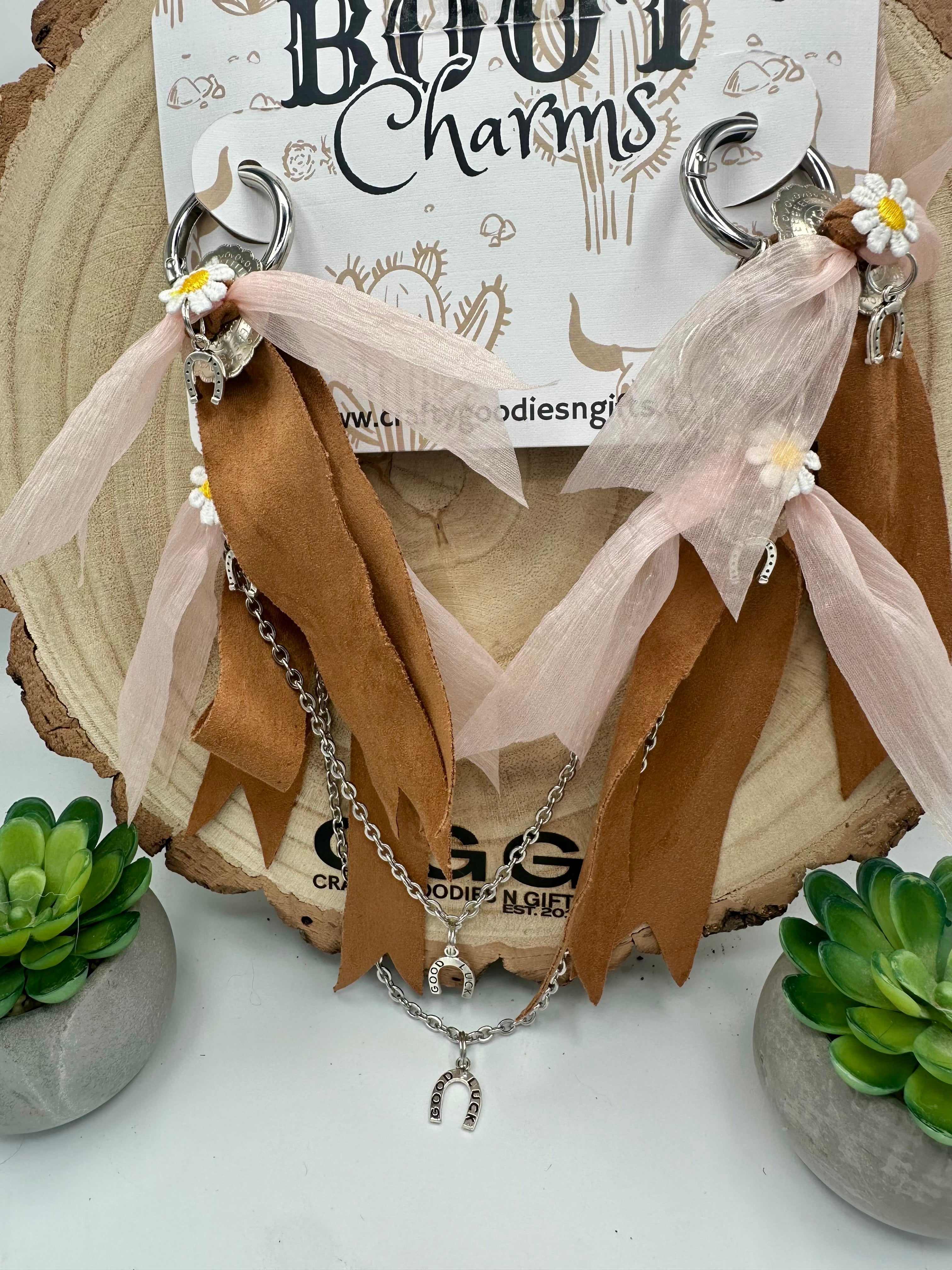A bohemian-style boot charms with silver-toned rings, brown suede-like ribbons, sheer blush pink tulle ribbons, small white daisy charms, and layered silver chains. 